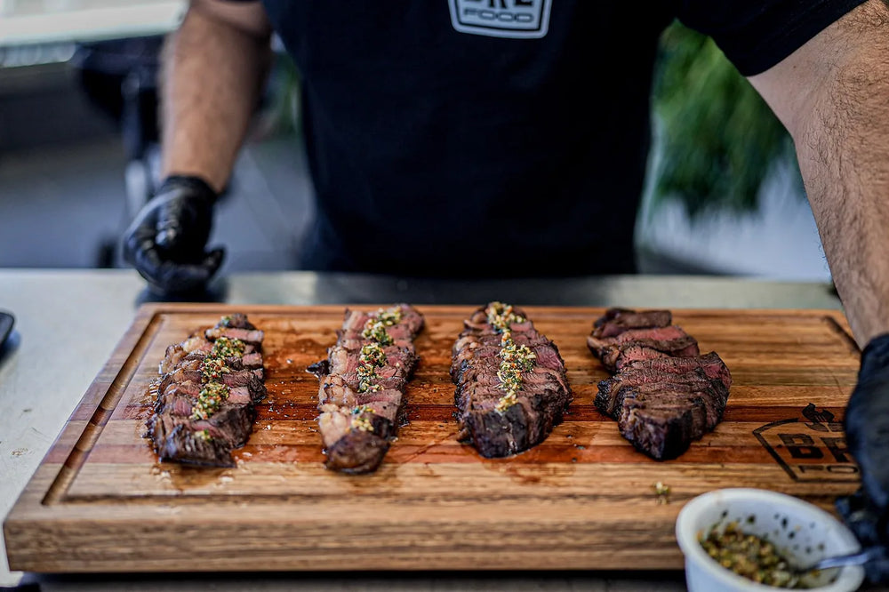 Picanha sliced and served on a board beside a bowl of chimichurri