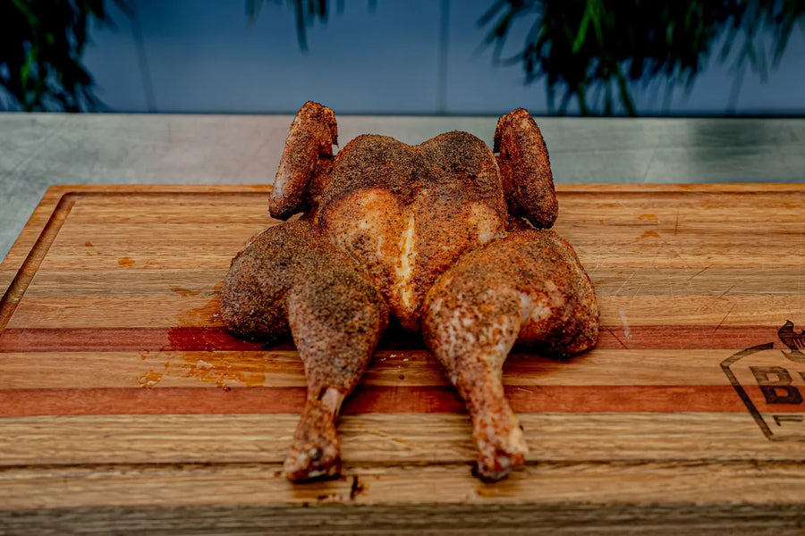 A butterflied chook, seasoned all over, resting on a timber board