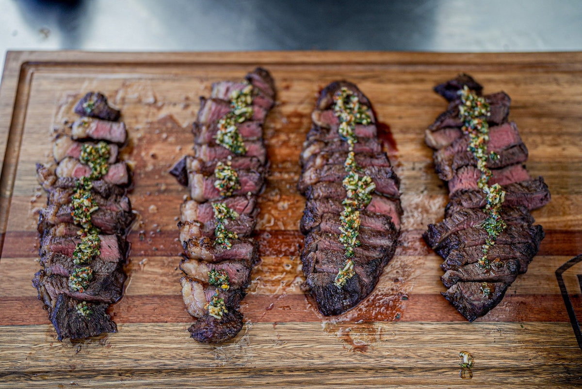 Ready to serve. Sliced picanha on a wooden board with chimichurri on top, dark crust and pink centre