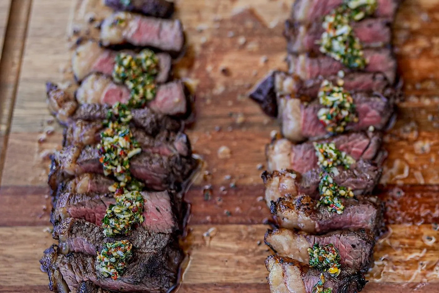 Sliced picanha with a herb topping on a wooden board
